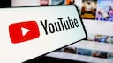 YouTube-Logo auf einem Smartphone mit Video-Thumbnails im Hintergrund