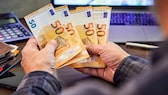 Mann hält mehrere 50-Euro-Banknoten in Händen