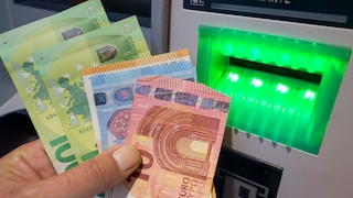 Person hält Bargeld vor einem Bankautomaten in der Hand