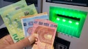 Person hält Bargeld vor einem Bankautomaten in der Hand