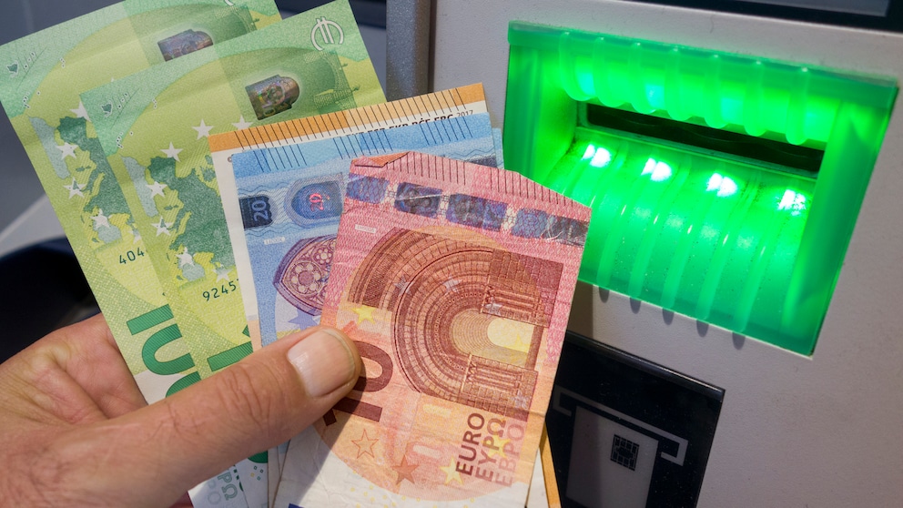 Person hält Bargeld vor einem Bankautomaten in der Hand