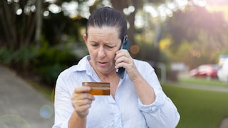 frau am Smartphone schaut besorgt auf ihre Kreditkarte