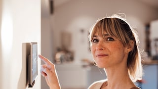 Frau bedient Smart-Home-Tablet an der Wand
