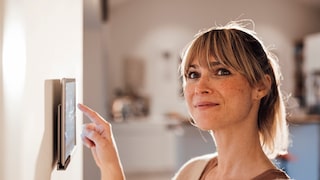 Frau bedient Smart-Home-Tablet an der Wand