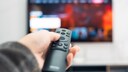Person zeigt mit Fernbedienung auf einen Fernseher