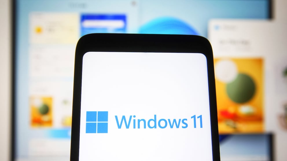 Windows 11 Logo auf einem Smartphone mit PC im Hintergrund