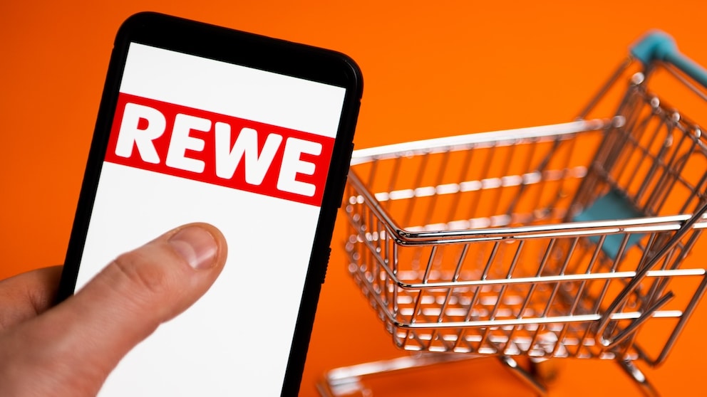 Rewe-Logo auf einem Smartphone, daneben ein Einkaufswagen