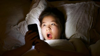 Mädchen liegt im Bett und schaut erschrocken aufs Smartphone