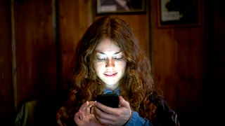 Frau schaut im Dunkeln auf ihr Smartphone