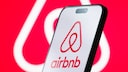 Airbnb-Logo auf einem Smartphone und im Hintergrund