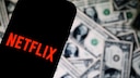 Netflix-Logo auf einem Smartphone, im Hintergrund US-Geld