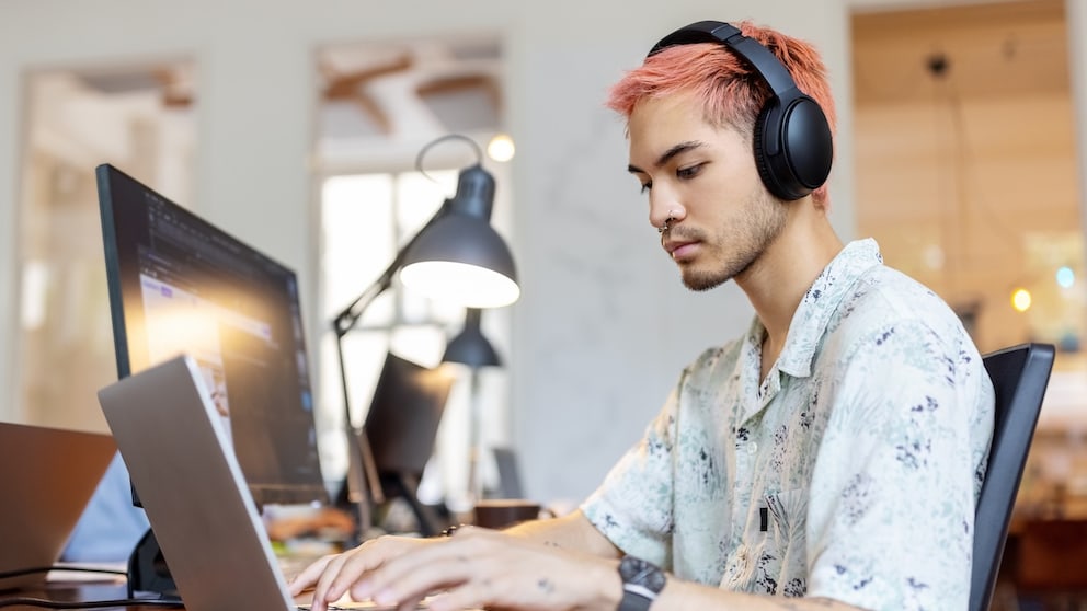Mann mit Bluetooth-Kopfhörer vor einem Laptop