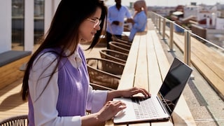 Frau arbeitet unter sonnigem, freien Himmel an ihrem Laptop