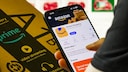 Person hält Amazon-Sendung in der Hand und hat Amazon offen auf dem Smartphone