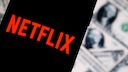 Netflix-Logo auf einem Smartphone, dahinter US-Dollar-Banknoten