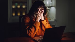 Frau sitzt mit vorgeschlagenen Händen am Laptop
