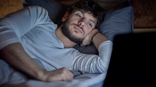 Mann schaut im Bett auf einen Laptop