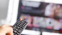 Person zeigt mit der Fernbedienung auf einen Fernseher