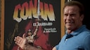 Arnold Schwarzenegger vor einem „Conan“-Poster