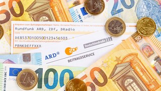 Unterlagen zum Rundfunkbeitrag und Bargeld auf einem Haufen