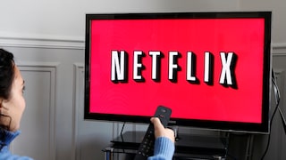 Frau hält Fernbedienung auf einen Fernseher mit Netflix