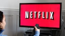 Frau hält Fernbedienung auf einen Fernseher mit Netflix