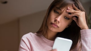 Frau schaut entnervt auf ihr Smartphone