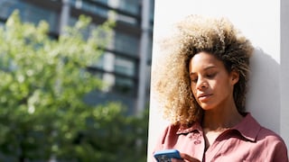 Frau in rosa Pulli steht gegen eine Wand gelehnt und schaut ernst aufs Handy
