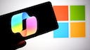 Smartphone mit Copilot Logo und Windows Logo im Hintergrund