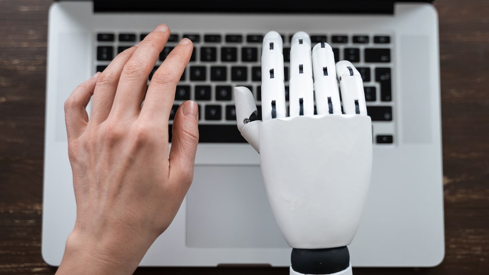 Roboter Hand und menschliche Hand die auf Computer tippen