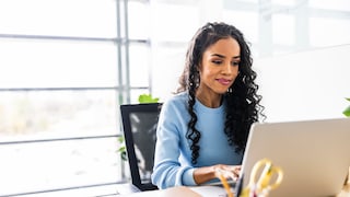 Frau in blauer Bluse sitzt vor dem Laptop