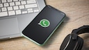 Smartphone mit WhatsApp-Logo neben Laptop und Kopfh&ouml;rern