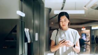 Asiatische Frau in weißer Bluse schaut auf ihr Smartphone