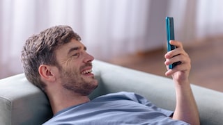 Mann liegt auf Sofa, schaut auf Smartphone