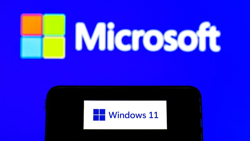 Smartphone zeigt Windows-11-Schriftzug vor Hintergrund mit Microsoft-Schriftzug