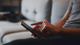 Mann auf Sofa tippt auf iPhone