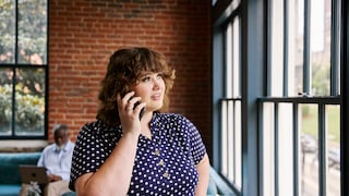 Frau in einem Café die aus dem Fenster schaut und telefoniert.