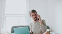 Ein w&uuml;tender Mann am Telefon, vor ihm ein Laptop