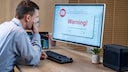 Mann vor PC auf dem eine Warnung angezeigt wird.