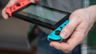 Mann mit einer Nintendo Switch in der Hand. Einer der Joy-Cons ist ein Stück oben heraus geschoben.