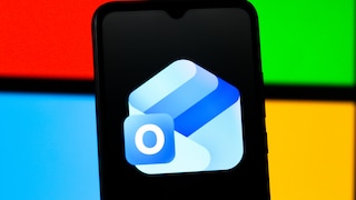 Smartphone mit Outlook-App-Logo auf schwarzem Display vor einem Hintergrund aus roten, grünen, blauen und gelben Farbflächen im Stil des Microsoft-Logos.