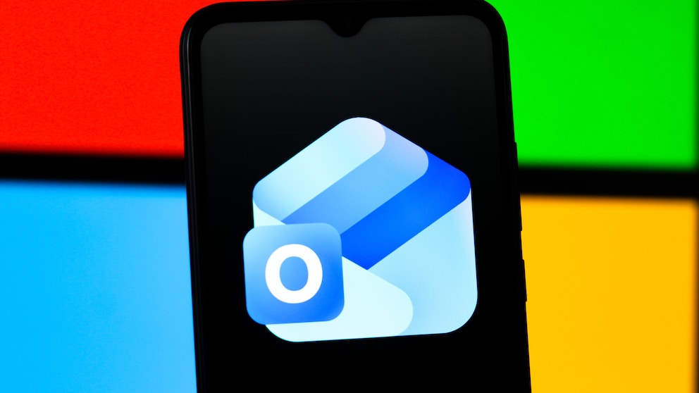 Smartphone mit Outlook-App-Logo auf schwarzem Display vor einem Hintergrund aus roten, grünen, blauen und gelben Farbflächen im Stil des Microsoft-Logos.