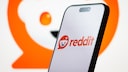 Smartphone mit Reddit-Logo im Vordergrund. Im Hintergrund ein gro&szlig;es Reddit-Logo.