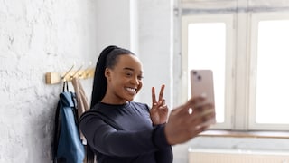 Junge dunkelhäutige Frau die ein Selfie macht und das Peace-Zeichen macht.