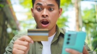 Mann schaut schockiert auf Kreditkarte und Smartphone.
