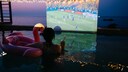 Person in Pool die auf gro&szlig;er Leinwand Fu&szlig;ball schaut