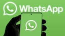 Eine Person h&auml;lt ein Smartphone auf dem ein gr&uuml;ner Bildschirm mit dem WhatsApp-Logo zu sehen ist. Der Hintergrund ist im gleichen gr&uuml;n mit einem zweiten WhatsApp-Logo.