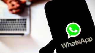 Smartphone mit WhatsApp-Logo im Vordergrund, im Hintergrund eine Person an einem Laptop.