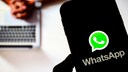 Smartphone mit WhatsApp-Logo im Vordergrund, im Hintergrund eine Person an einem Laptop.