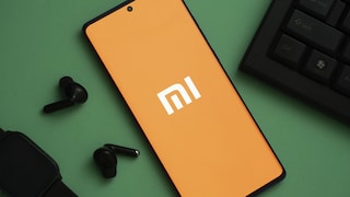 Smartphone mit Xiaomi-Logo auf grünem Untergrund. Daneben die Ecke eines Laptops und lose In-Ear-Kopfhörer.